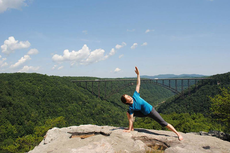 Dr. Sweet in yoga pose on top of mountain with trees in gorge and trees in background