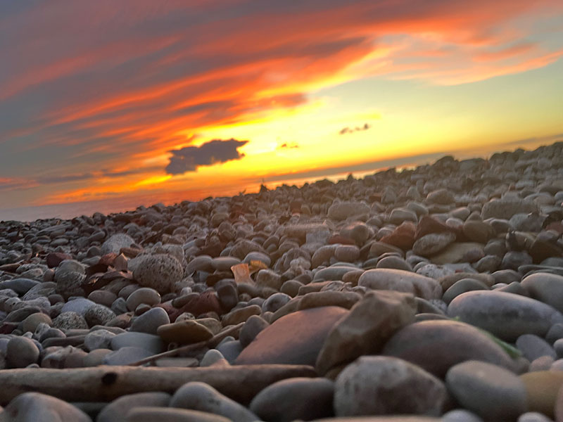 Orange skyline with clouds and layers of rocks on a beach; Physical Therapy