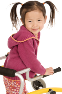 Girl with pony tails and pink shirt smiling in her walker.