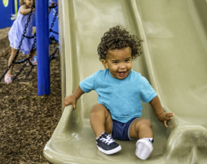 Little boy wearing blue shirt while seated on a slide. Change your child's life with intensive physical therapy.