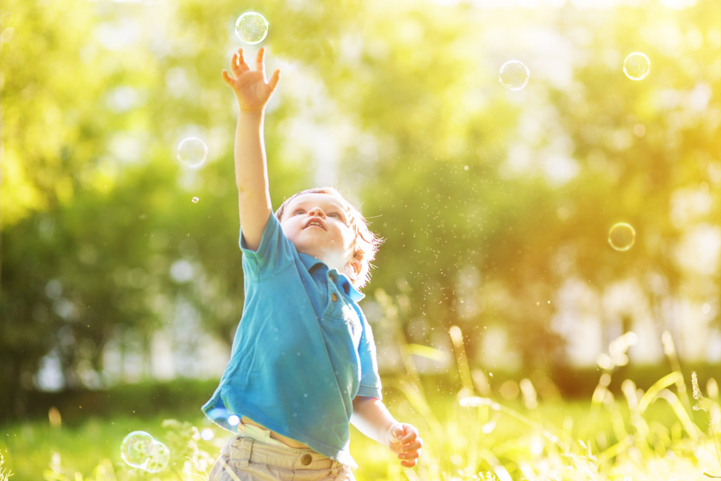 Little boy popping bubbles with one hand while outside.